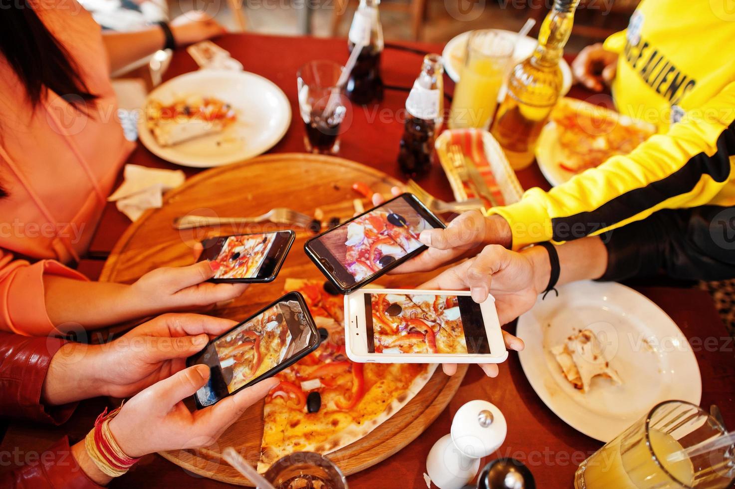 hände von freunden, die während der party in der pizzeria foto mit dem handy von pizza machen. glückliche menschen, die zusammen spaß haben.