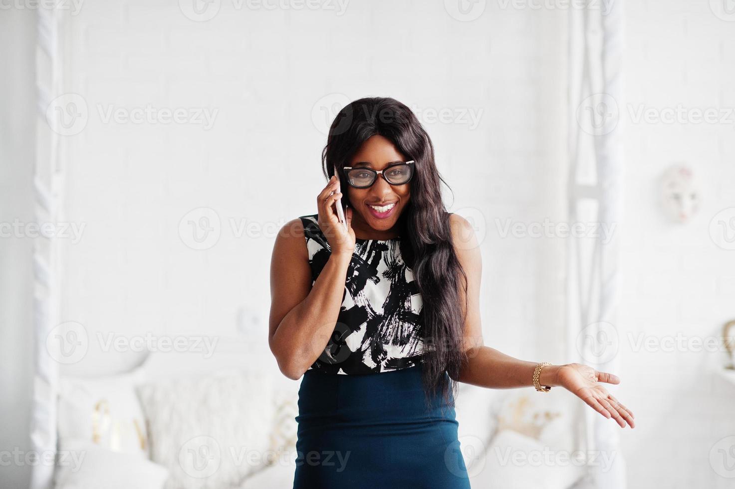 hübsche afroamerikanische frau mit brille posierte im zimmer mit handy zur hand. foto