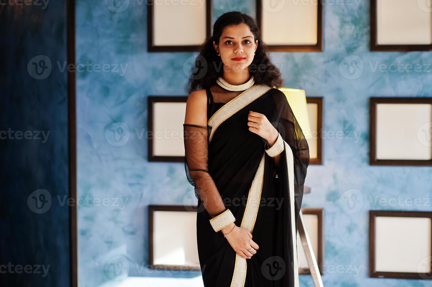 junge inderin trägt einen eleganten schwarzen saree, der im restaurant an der wand mit rahmen posiert. foto