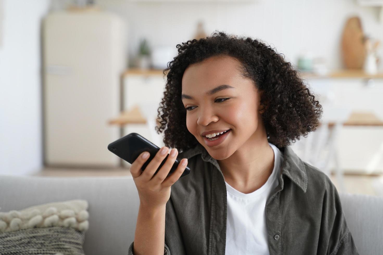 freundliches afroamerikanisches junges mädchen hält smartphone und hinterlässt eine sprachnachricht oder verwendet einen virtuellen assistenten foto