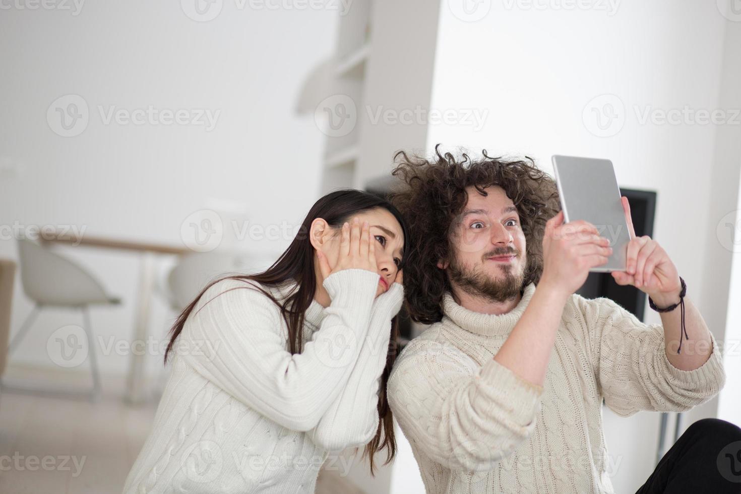 Multiethnisches Paar mit Tablet-Computer vor dem Kamin foto
