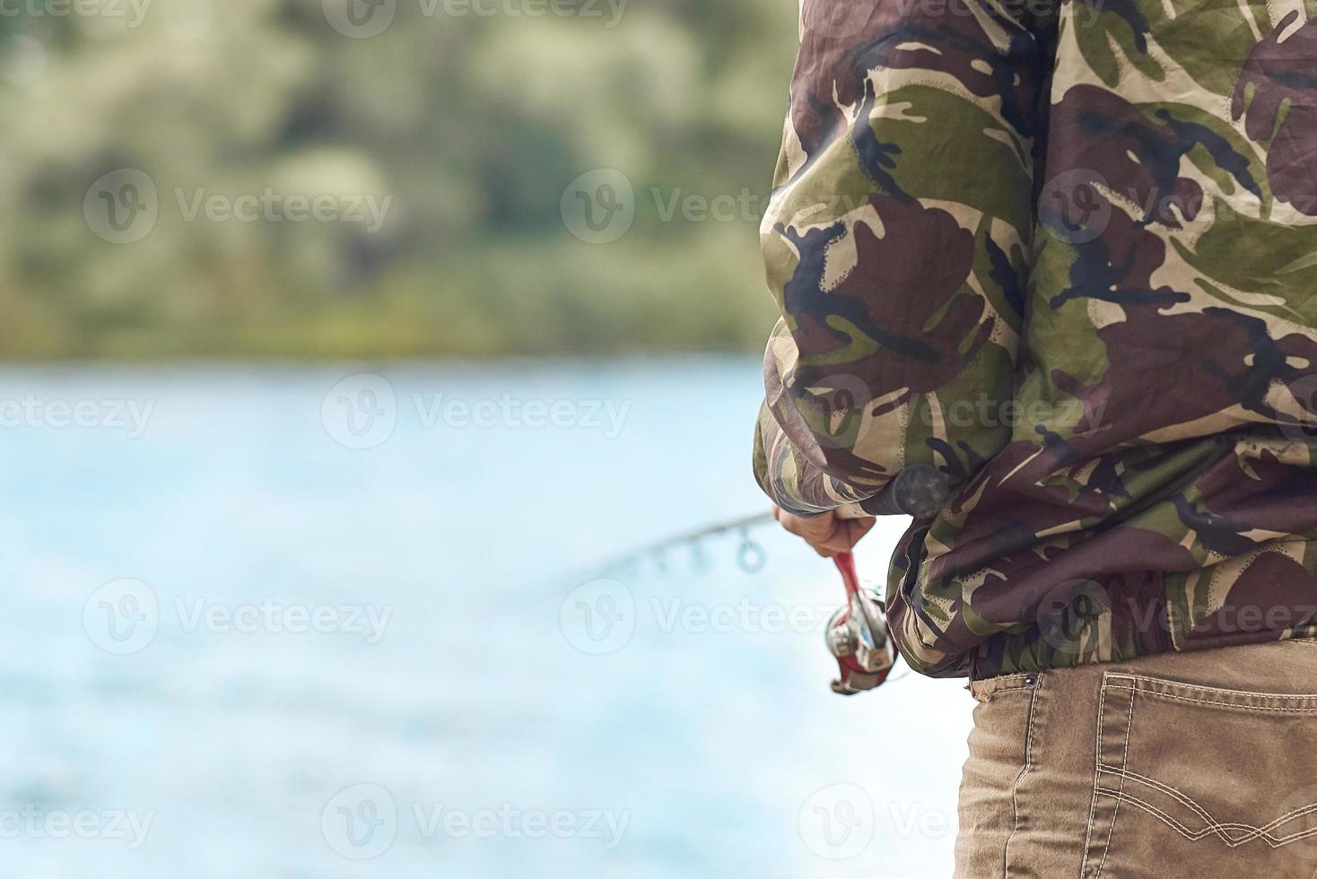 Fischer, der mit Spinnrute an einem Flussufer vor dem Hintergrund des Wassers in Unschärfe fischt. foto