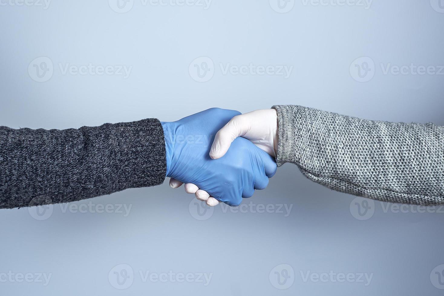 Händeschütteln in medizinischen Handschuhen auf grauem Hintergrund. das Konzept eines sicheren Händedrucks. foto