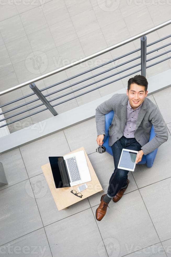junger asiatischer Geschäftsmann mit Tablette, Handy im Büro foto