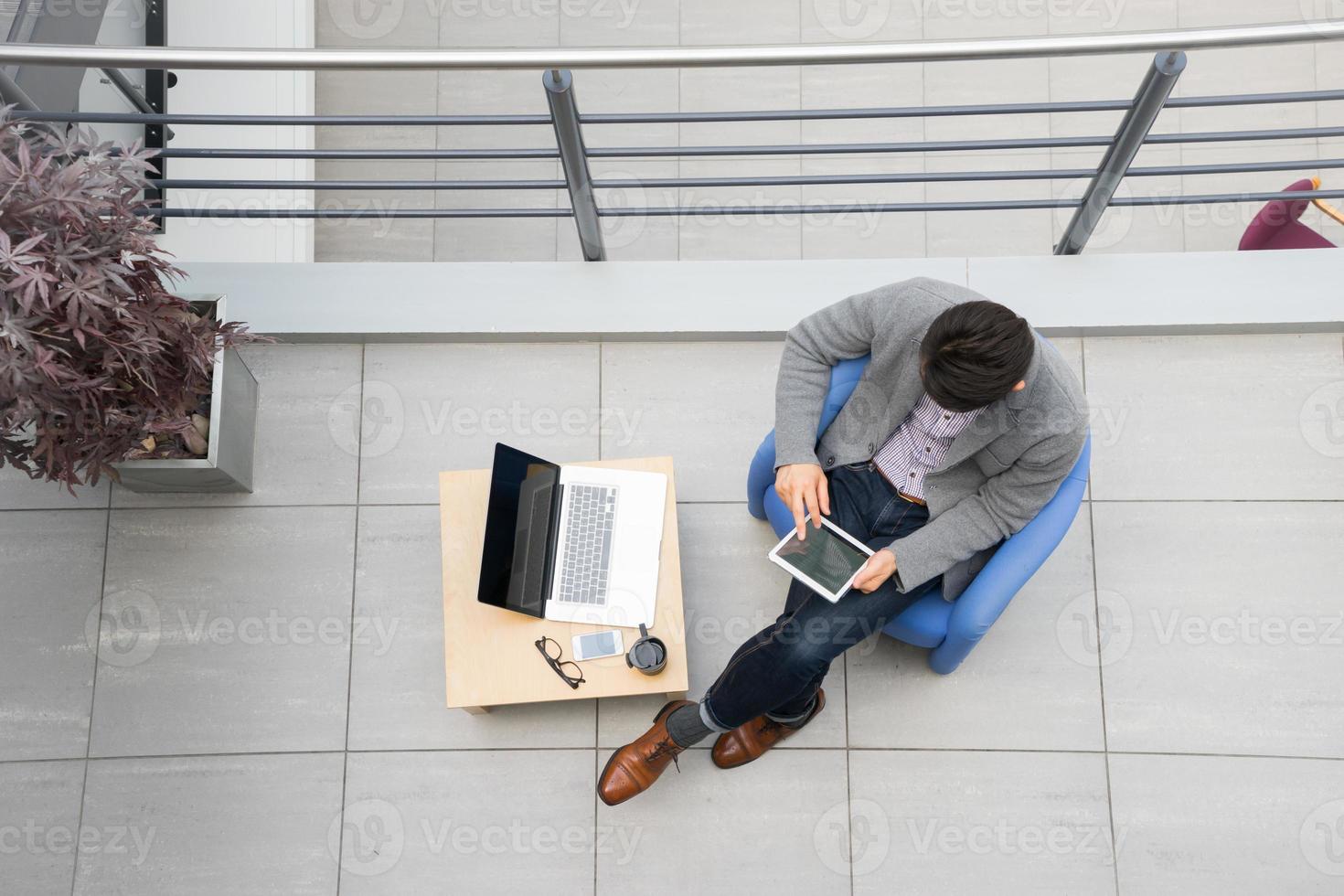 junger asiatischer Geschäftsmann mit Tablette, Handy im Büro foto