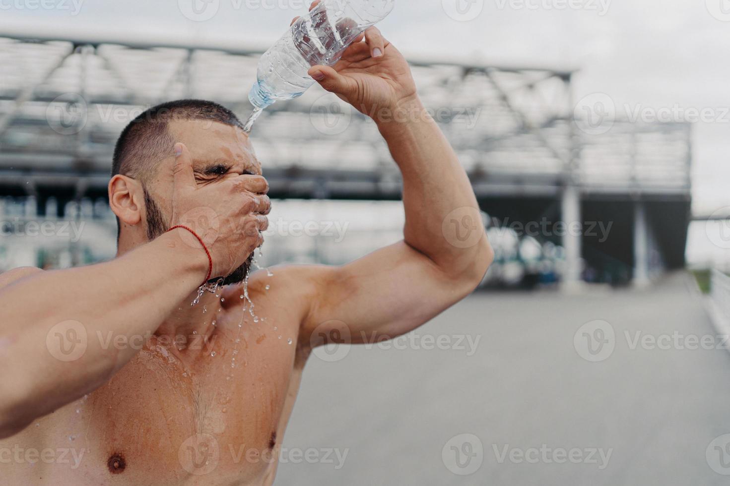 bild eines athletischen kerls mit muskulösem körper gießt sich wasser aus der flasche auf, erholt sich nach einem harten training, fühlt sich müde und durstig, kühlt den körper mit kalter flüssigkeit, liebt sport. gesunder Lebensstil foto