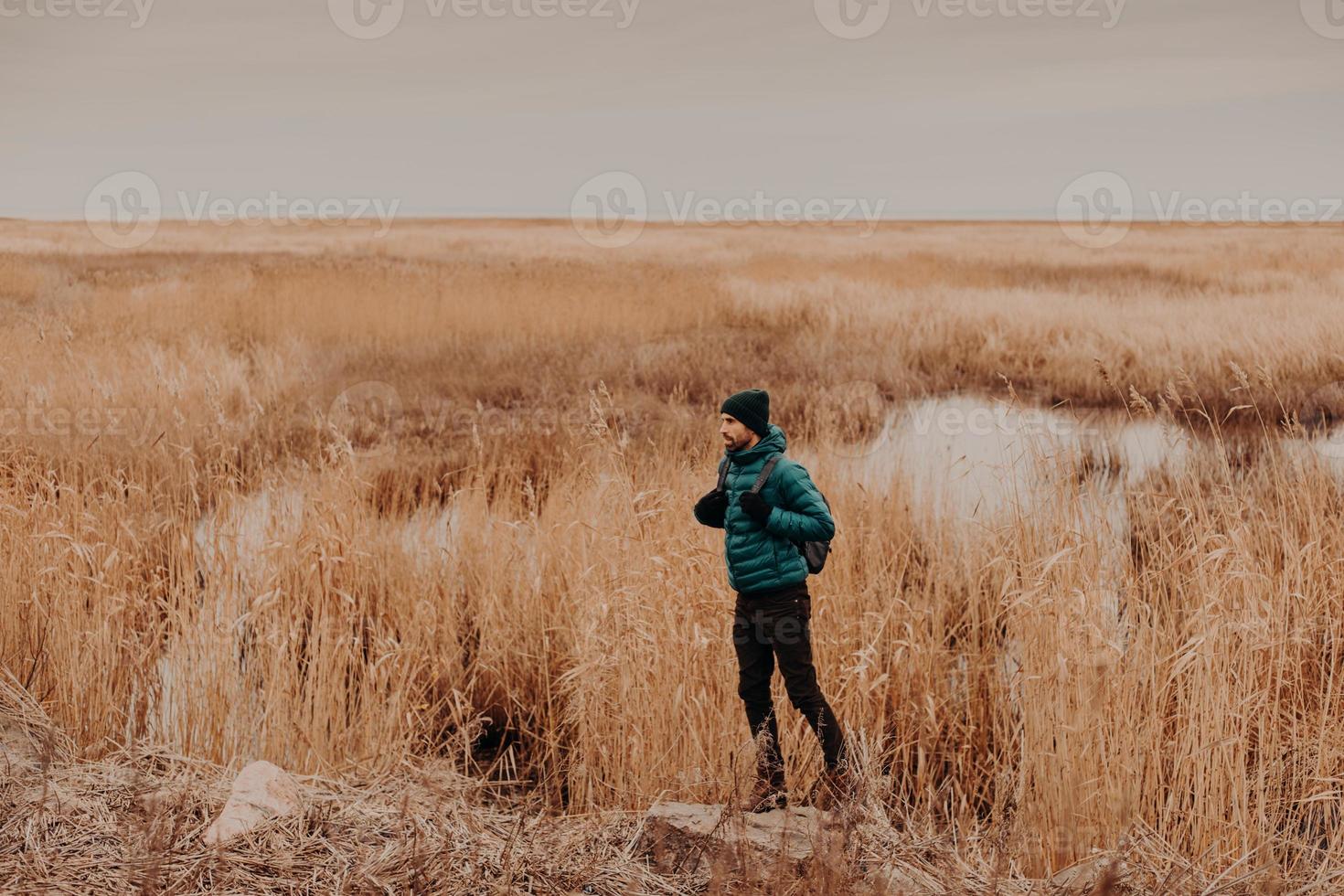 seitliches Foto eines attraktiven Mannes mit modischem Hut, Jacke und Hose, trägt einen Rucksack, steht im Freien, hat eine unvergessliche Reise, genießt die Herbstzeit. Menschen, Ruhe und Lifestyle-Konzept