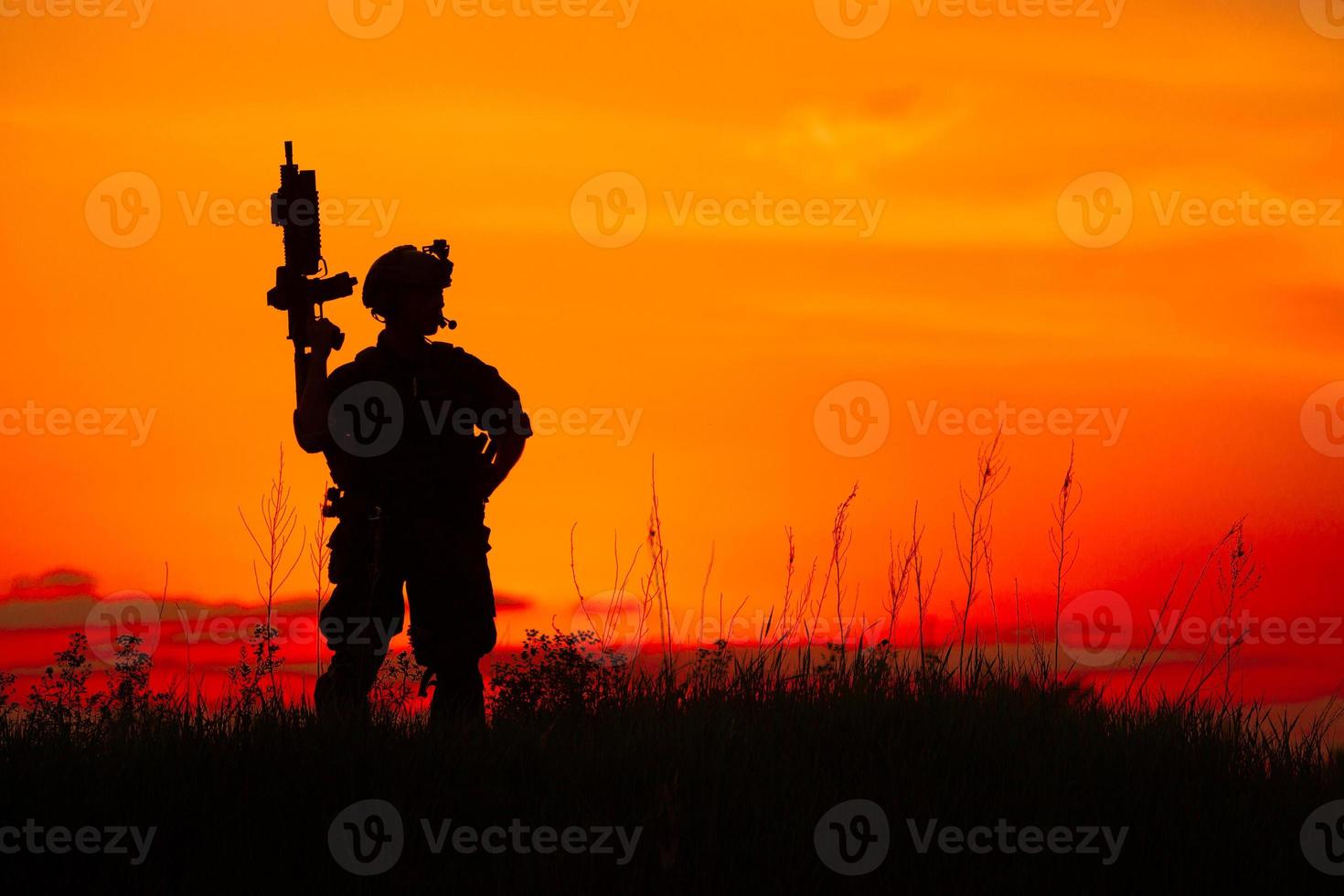 Silhouette des Militärsoldaten oder des Offiziers mit den Waffen bei Sonnenuntergang foto