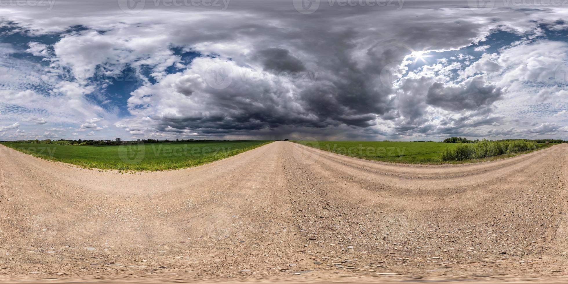 Vollständiges, nahtloses sphärisches HDRI-Panorama 360-Grad-Winkelansicht auf verkehrsfreier Schotterstraße zwischen Feldern mit bewölktem Himmel vor Sturm in gleichrechteckiger Projektion, bereit für VR- und Virtual-Reality-Inhalte foto