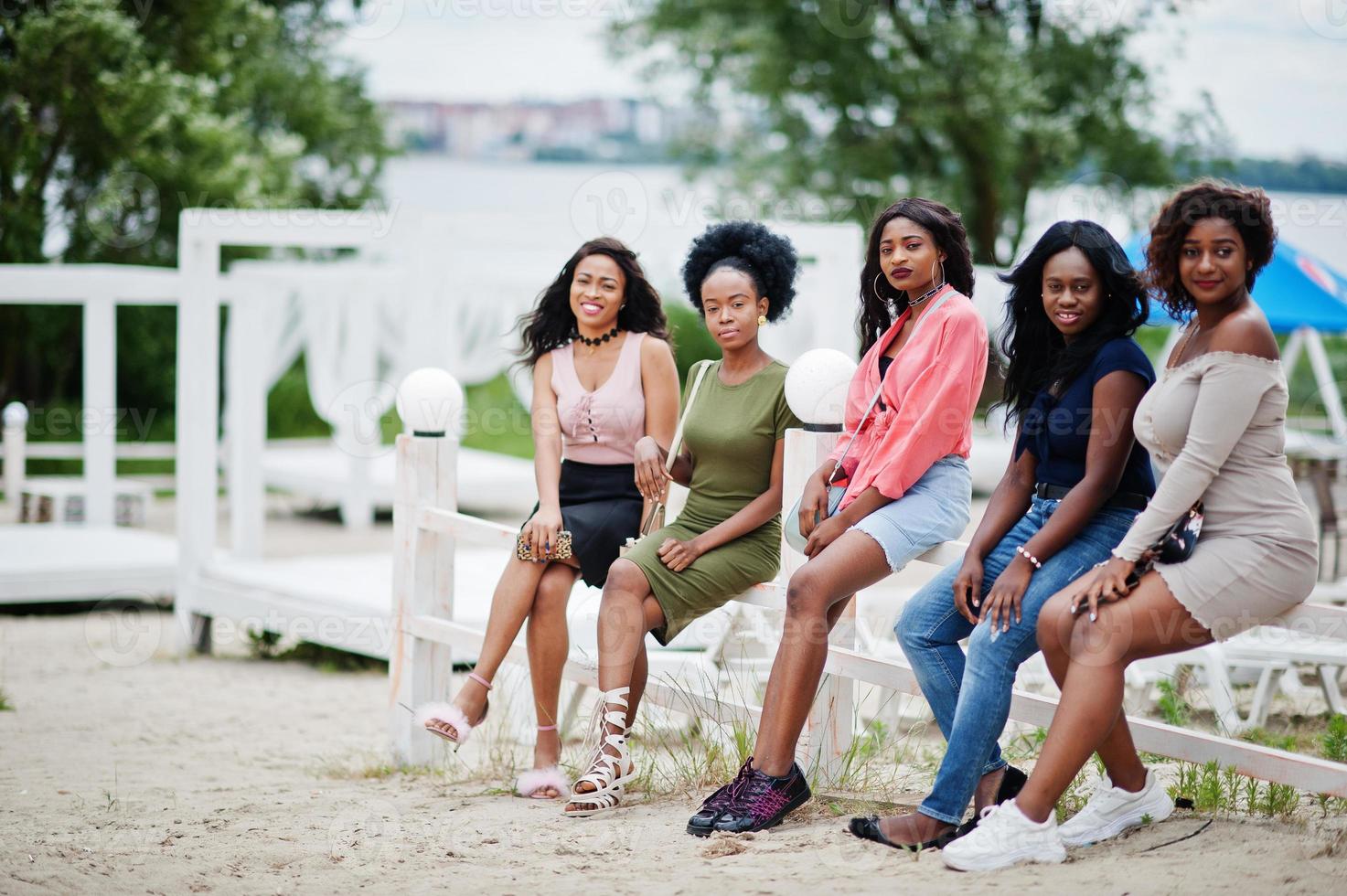 Gruppe von fünf afroamerikanischen Mädchen, die sich in der wunderschönen Cabana am Pool neben dem Luxusresort entspannen. foto