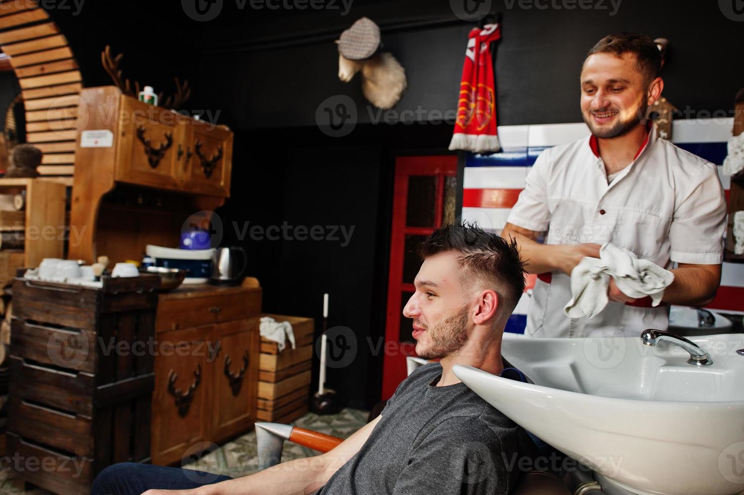 Junger bärtiger Mann, der den Kopf vom Friseur wäscht, während er im Friseursalon auf dem Stuhl sitzt. Barbier Seele. foto