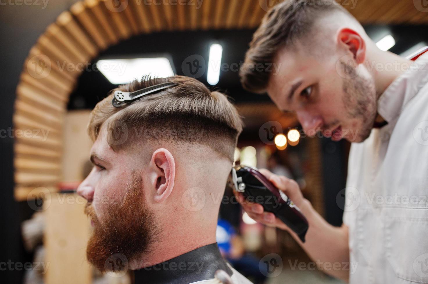 junger bärtiger mann, der vom friseur die haare schneiden lässt, während er im friseursalon auf dem stuhl sitzt. Barbier Seele. foto