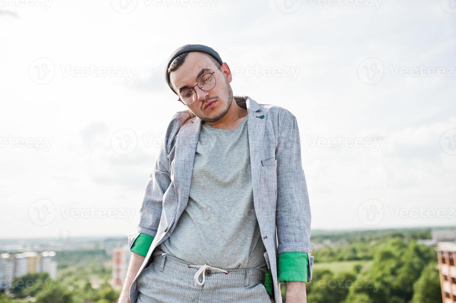 träumer stylischer machomann in grauem anzug, hut und brille posierte auf dem dach. foto