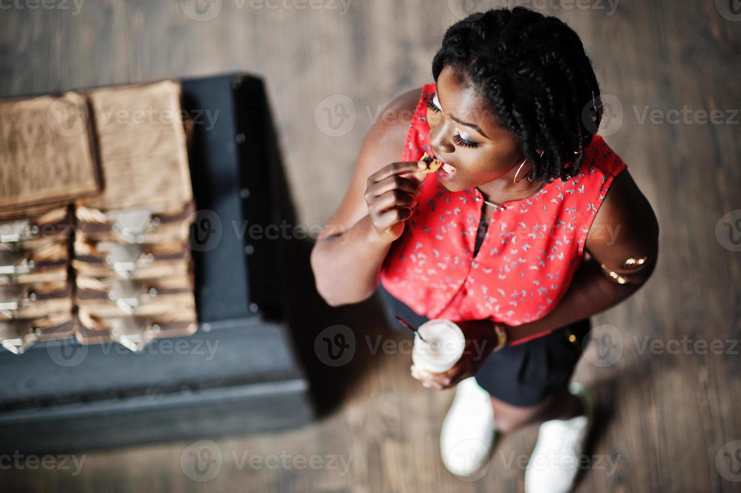 Attraktives afroamerikanisches Mädchen posierte im Café mit Latte und Plätzchen zur Hand. Sicht von oben. foto