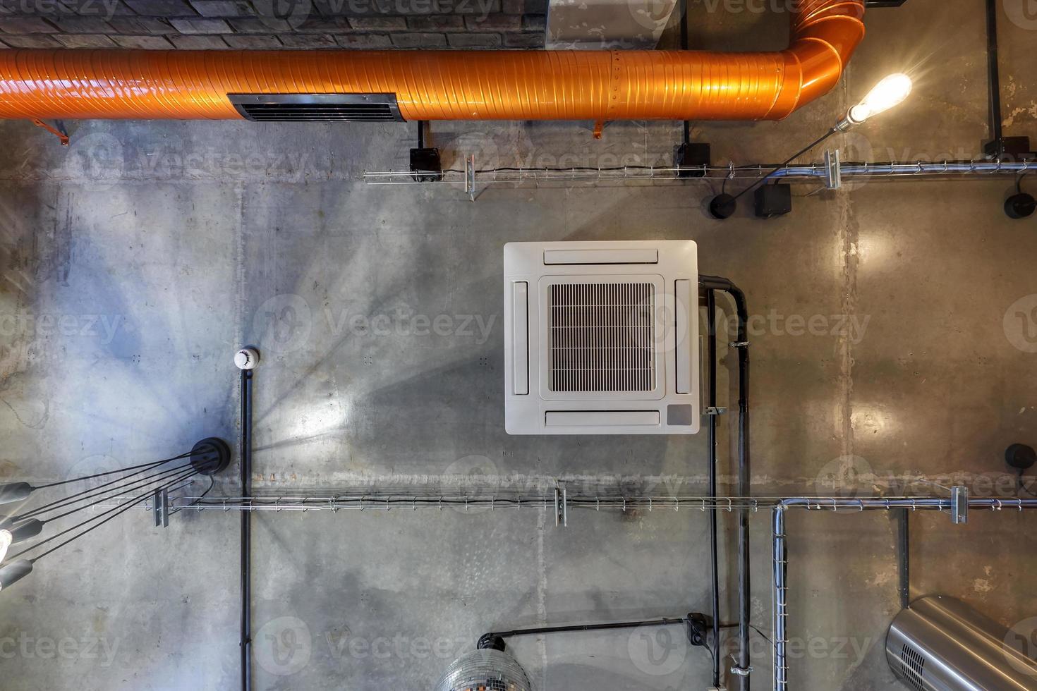 Blick nach oben auf graue Betondecke mit Halogenspots und Edison-Lampen im Loft-Büroraum mit Klimaanlage und orangefarbenem Lüftungsrohr foto