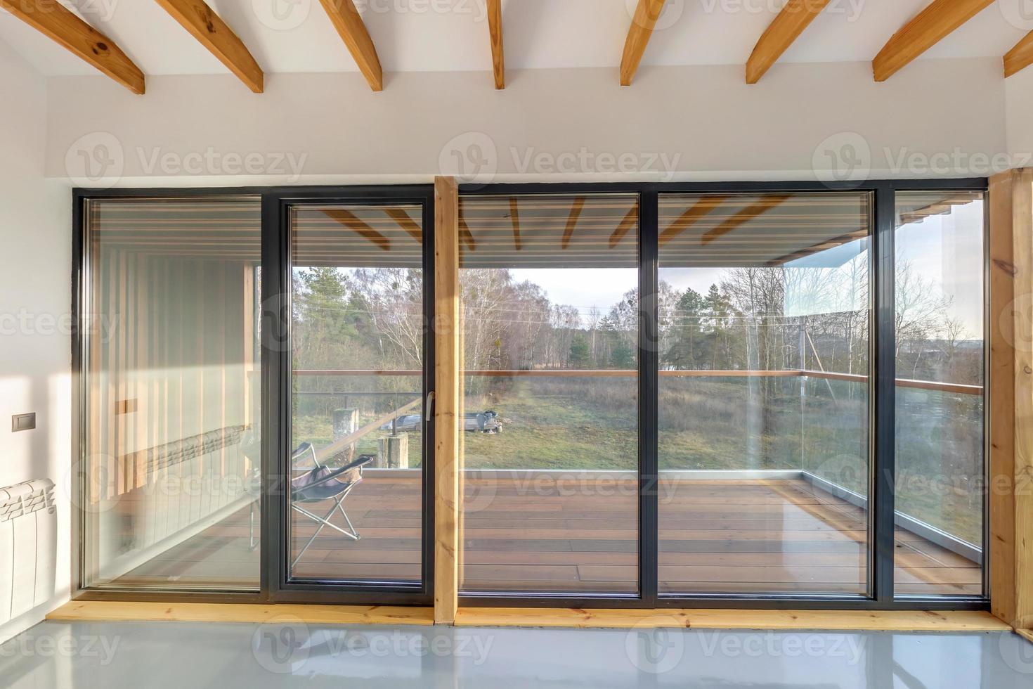 Weiße, leere Wohnung mit Panoramafenstern und Holzsparrendecke im Ferienhaus, mit Blick auf die Natur im Wald foto