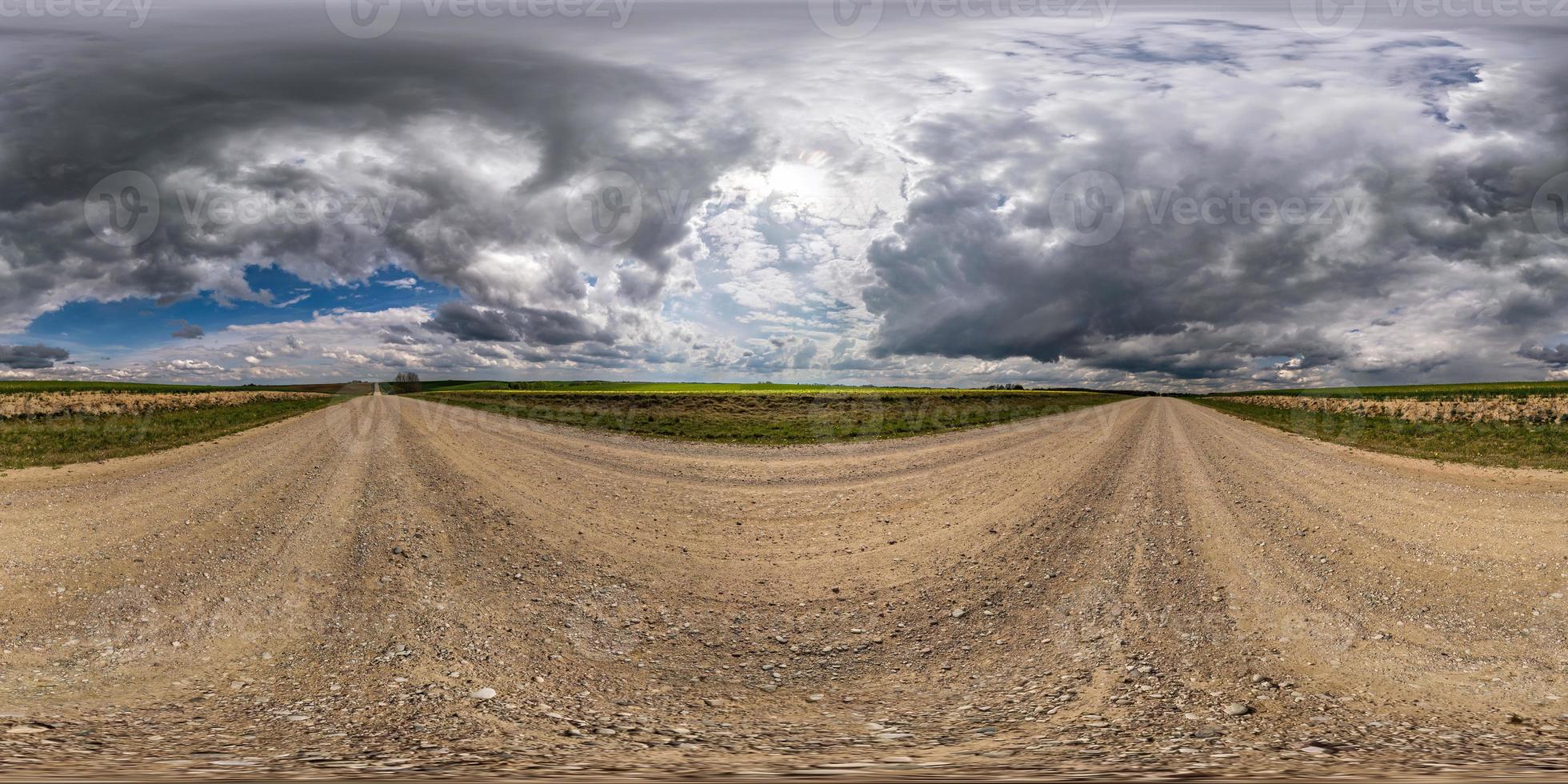 Vollständiges, nahtloses sphärisches HDRI-Panorama 360-Grad-Winkelansicht auf Schotterstraße zwischen Feldern am Frühlingstag mit Gewitterwolken vor Regen in equirectangularer Projektion, bereit für VR-AR-Inhalte foto