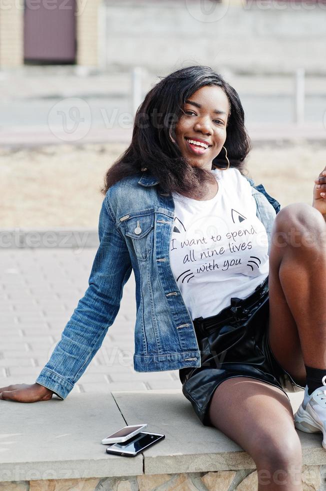 afroamerikanisches, dunkelhäutiges, schlankes Model posiert in schwarzen Shorts und Jeansjacke mit Handy. foto