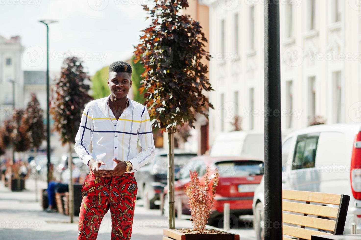 Porträt eines hübschen, stilvollen afroamerikanischen Modellmanns in roten Hosen und weißem Hemd mit Handy zur Hand. foto