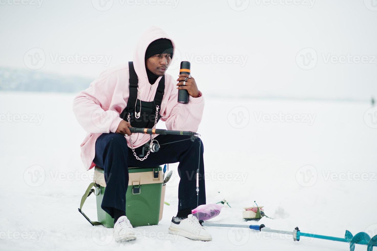 Afroamerikanischer Fischer mit Angelrute und Thermoskanne. Winterangeln. foto