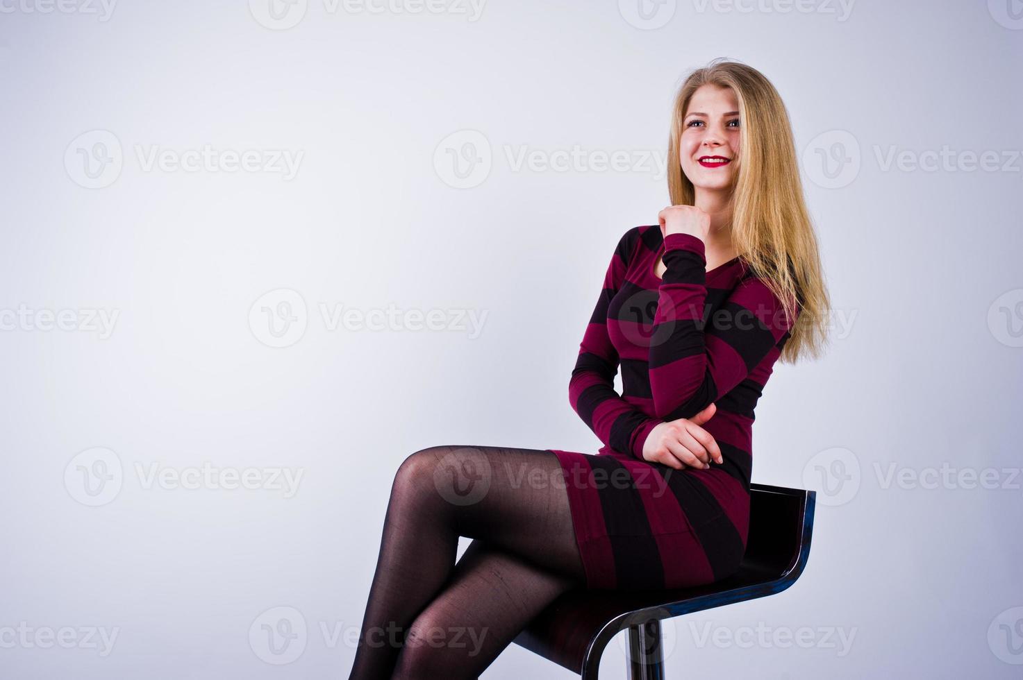 Porträt einer jungen Frau in gestreiftem lila Kleid, die auf dem Stuhl im Studio sitzt. foto