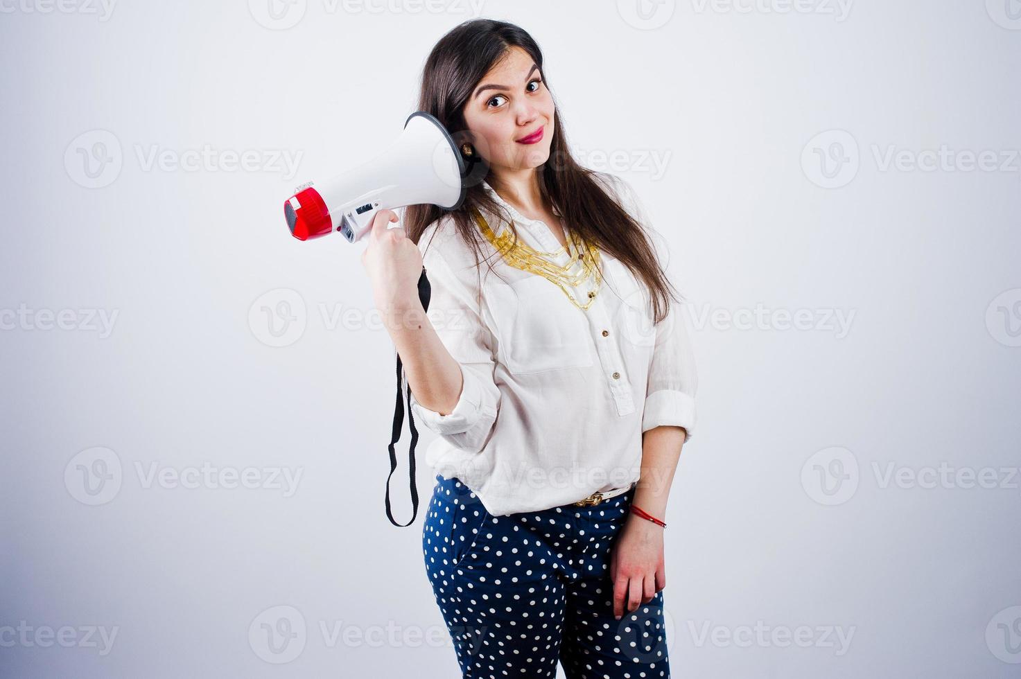 Porträt einer jungen Frau in blauer Hose und weißer Bluse, die im Studio mit Megaphon posiert. foto