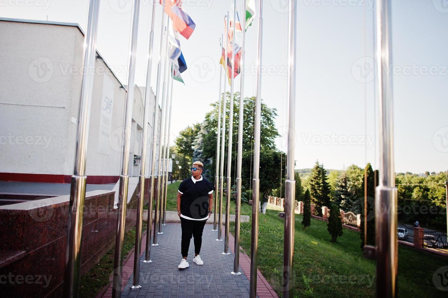 Stilvoller arabischer muslimischer Junge mit ursprünglich auf Straßen gestellten Haaren, gegen Flaggen verschiedener Länder. foto