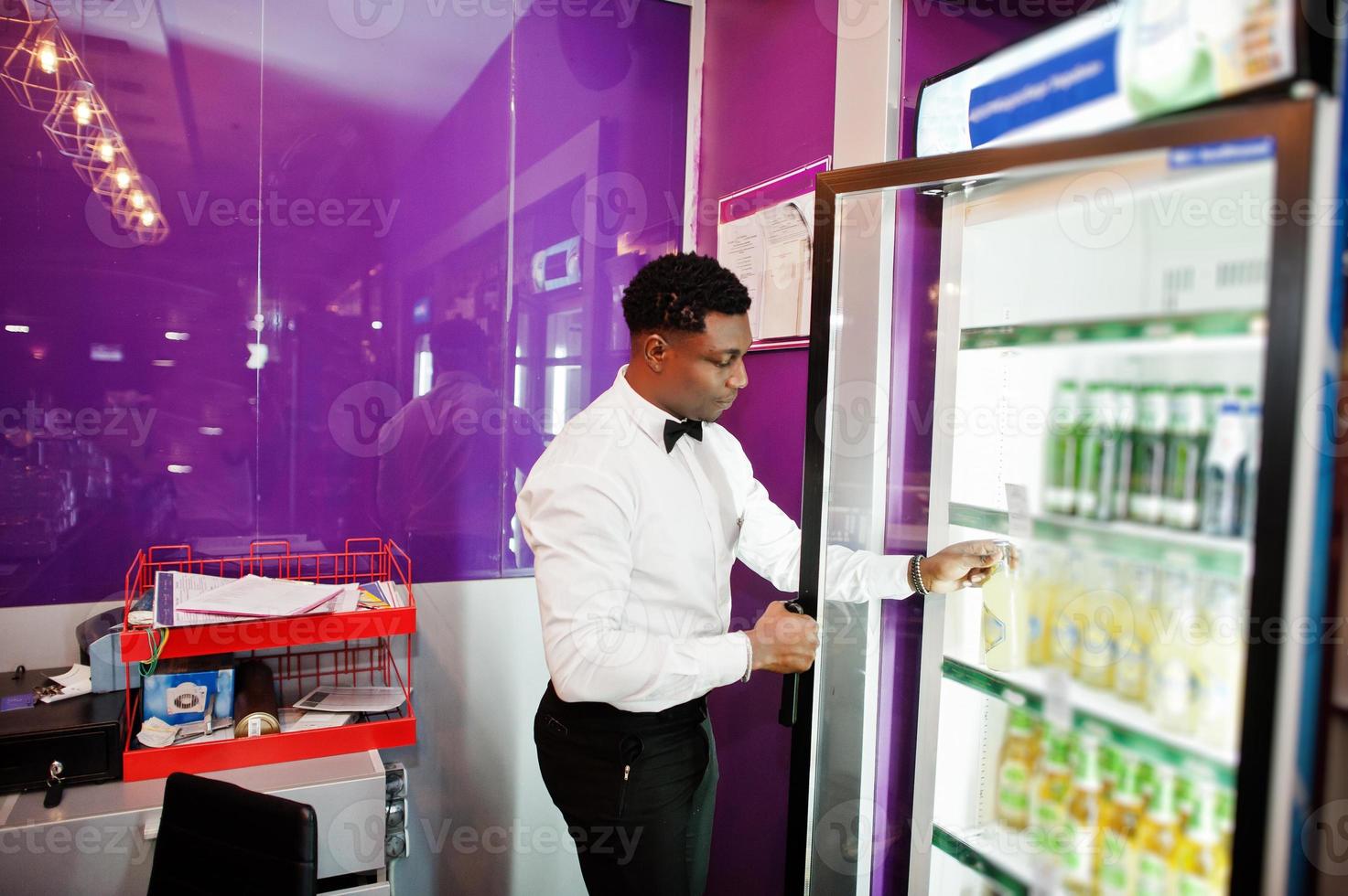 afroamerikanischer barkeeper an der bar, der bier aus dem kühlschrank nimmt. foto