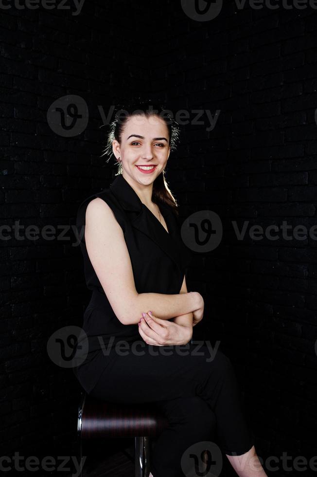 Porträt eines schönen brünetten Mädchens im schwarzen Overall, das im Studio sitzt und posiert. foto