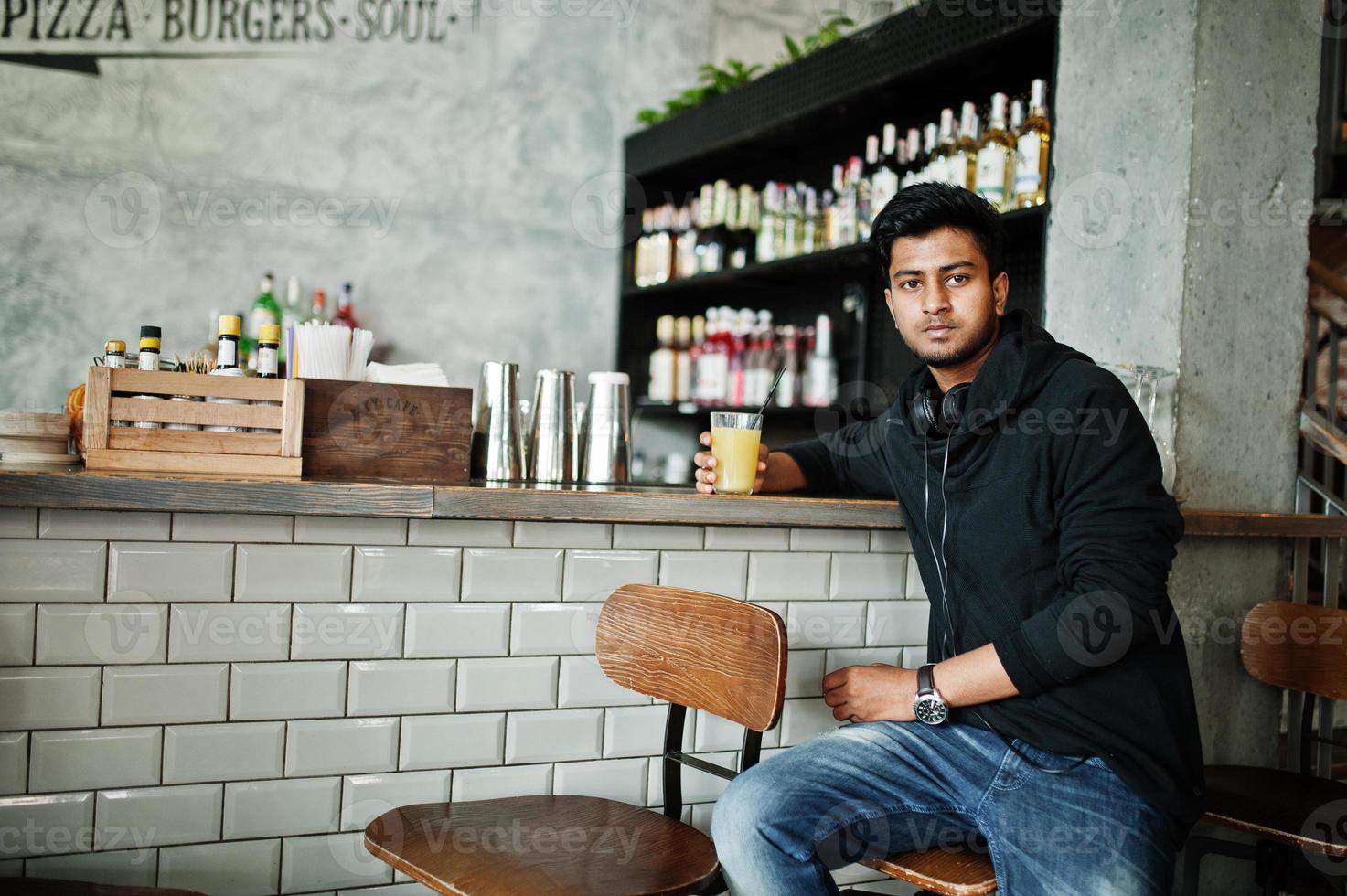 Lässiger und stilvoller junger asiatischer Mann mit Kopfhörern im Café an der Bar, der Saft aus Glas trinkt. foto