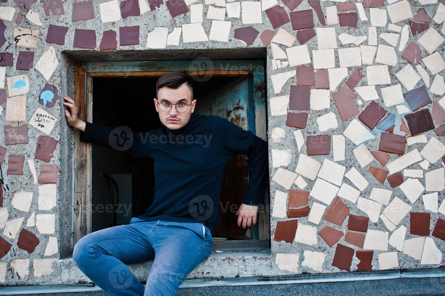 Träumer stylischer Macho in schwarzem Golf und Brille posiert auf dem Dach. foto