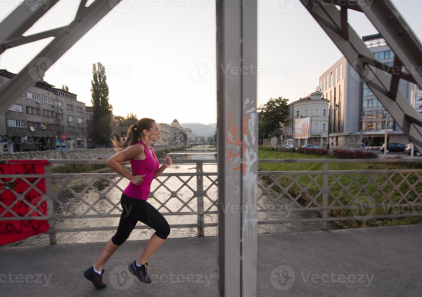 Frau, die am sonnigen Morgen über die Brücke joggt foto