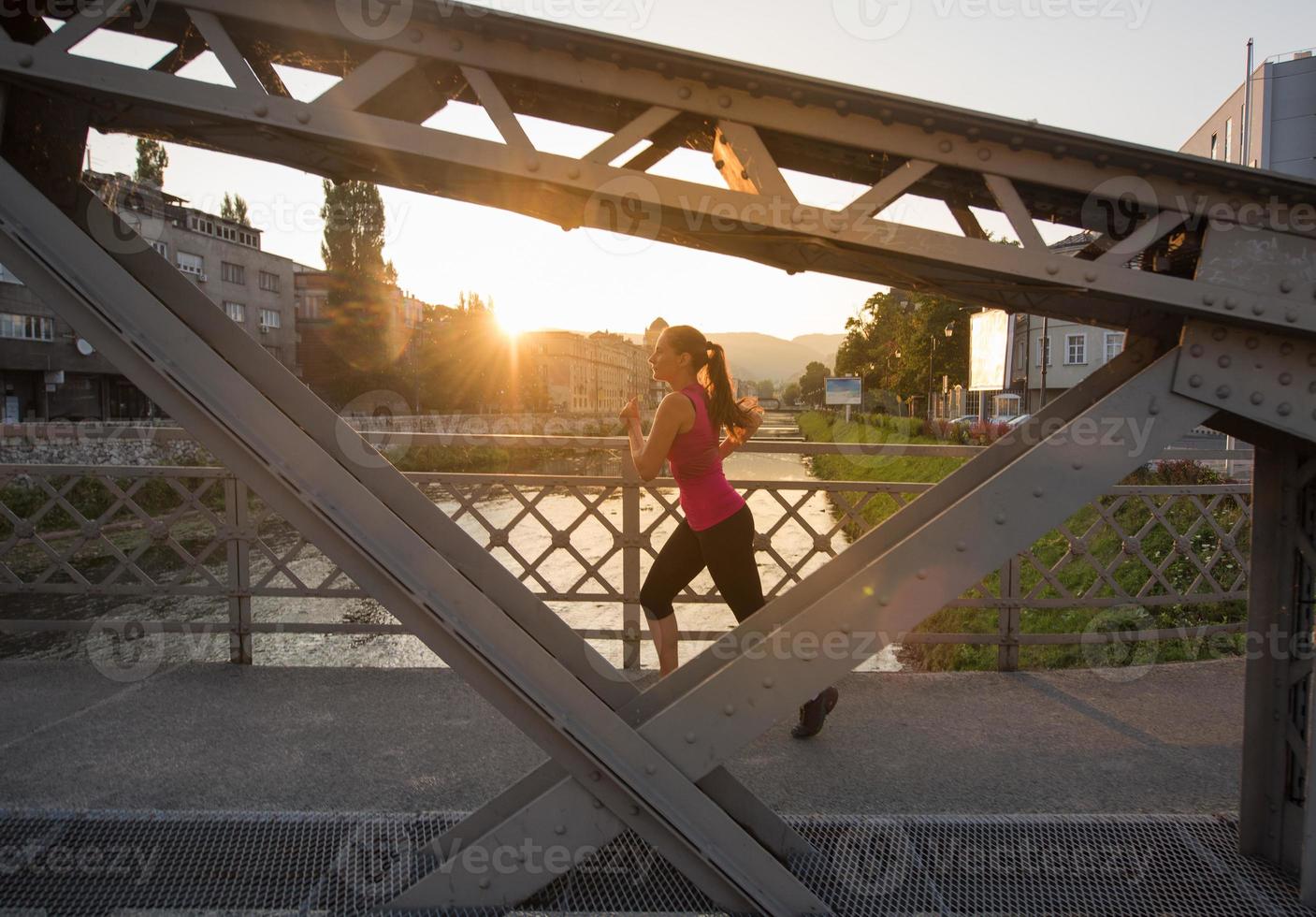 Frau, die am sonnigen Morgen über die Brücke joggt foto