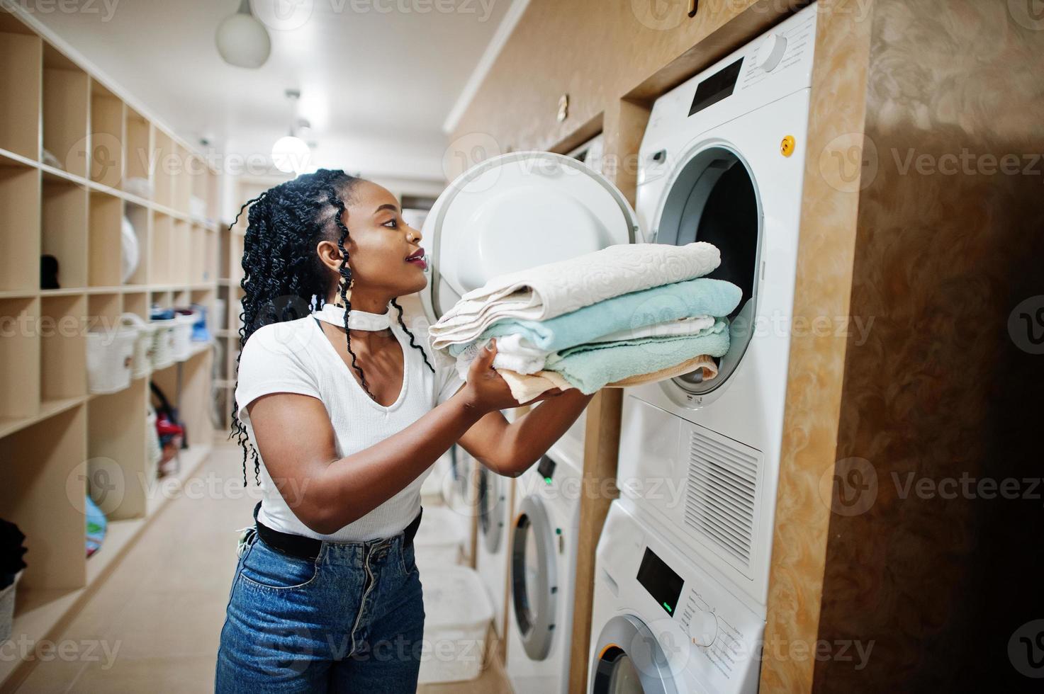 Fröhliche afroamerikanische Frau mit Handtüchern in der Nähe der Waschmaschine in der Selbstbedienungswäscherei. foto