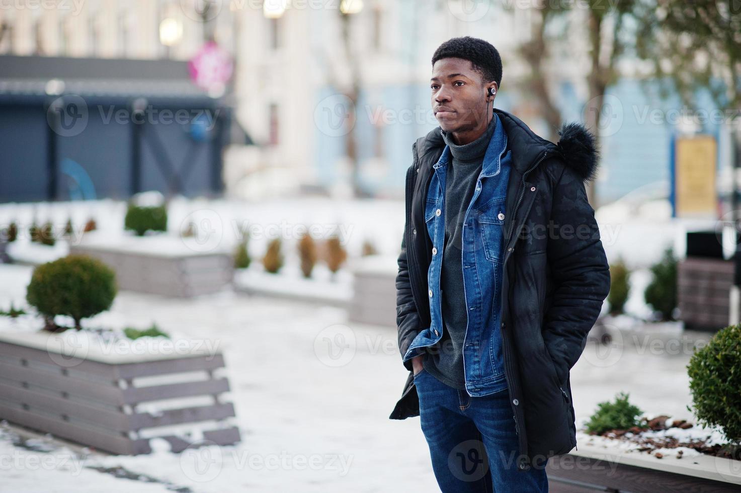 afrikanischer mann trägt jacke bei kaltem winterwetter im freien mit kopfhörern an den ohren. foto