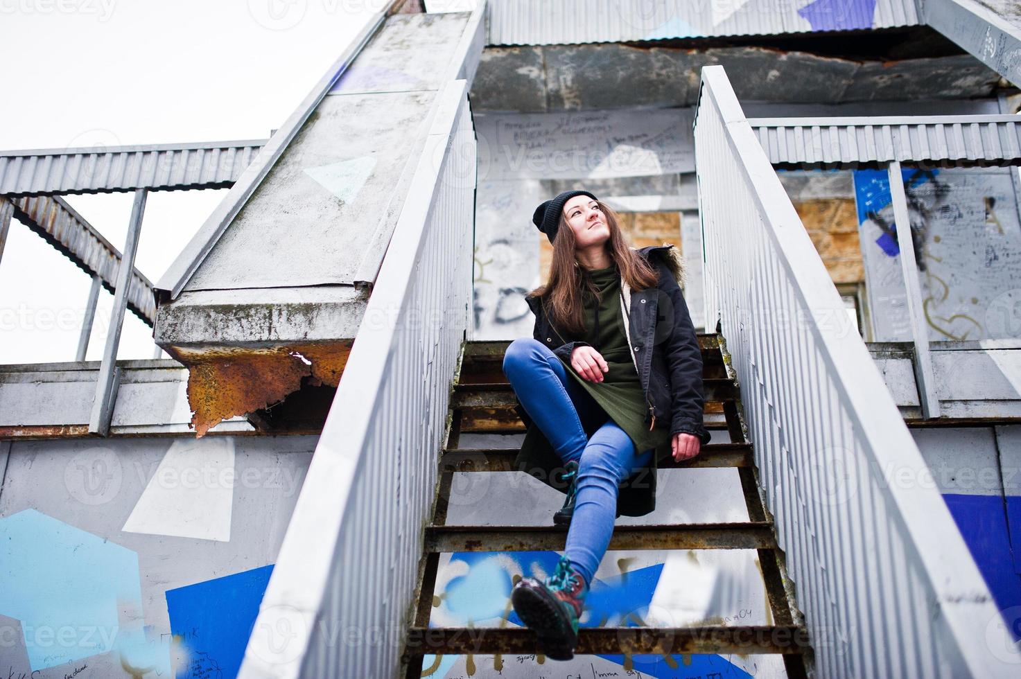 junge mädchen tragen ein langes grünes sweatshirt, jeans und schwarze kopfbedeckungen an einem industrieplatz. foto