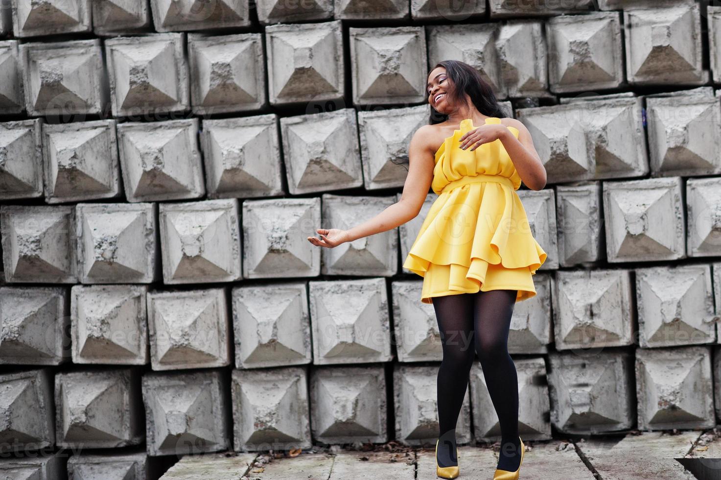 stilvolle afrikanisch-amerikanische Frau im gelben Kleid posierte vor steinernem Hintergrund. foto