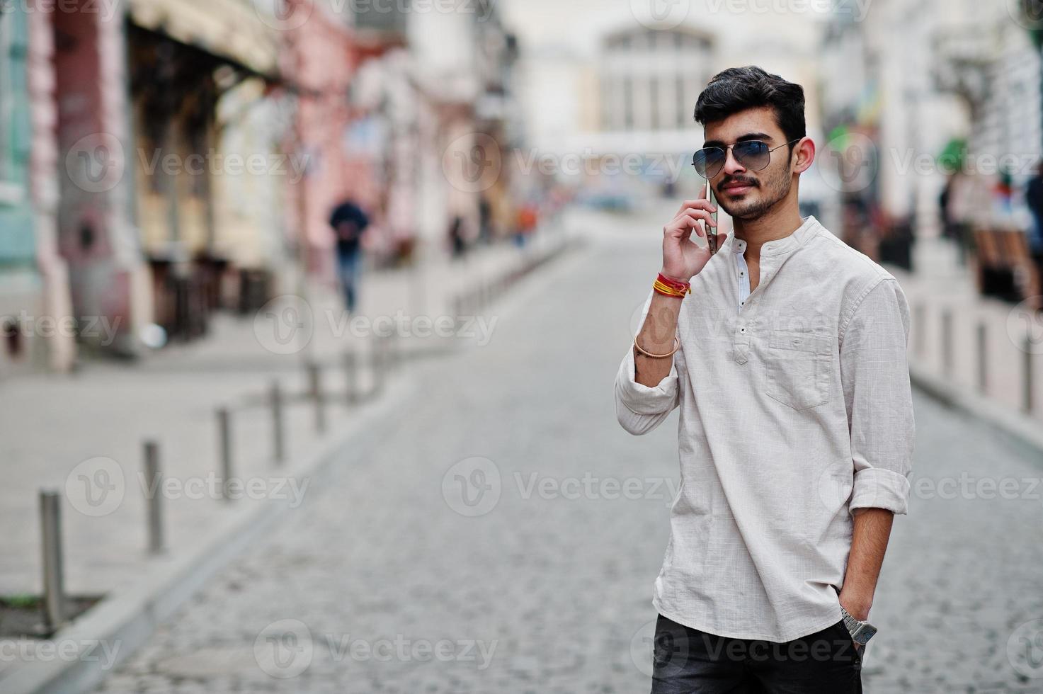 Stilvoller indischer Modellmann in Freizeitkleidung und Sonnenbrille posierte im Freien auf der Straße von Indien und telefonierte mit dem Handy. foto