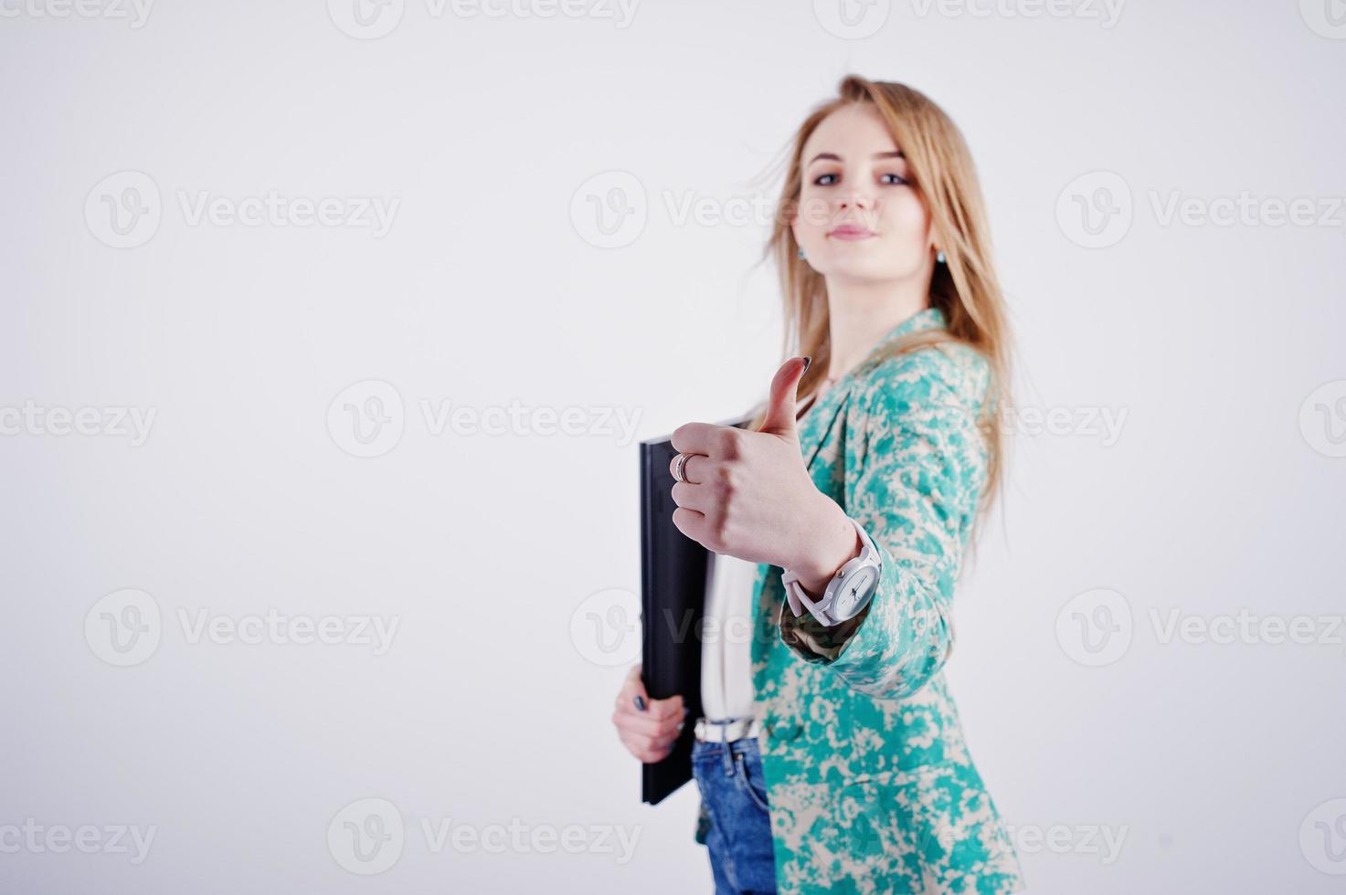 Stilvolles blondes Mädchen in Jacke und Jeans mit Notizbuch, Tagebuch und Laptop an den Händen, die Daumen nach oben vor weißem Hintergrund im Studio zeigen. foto