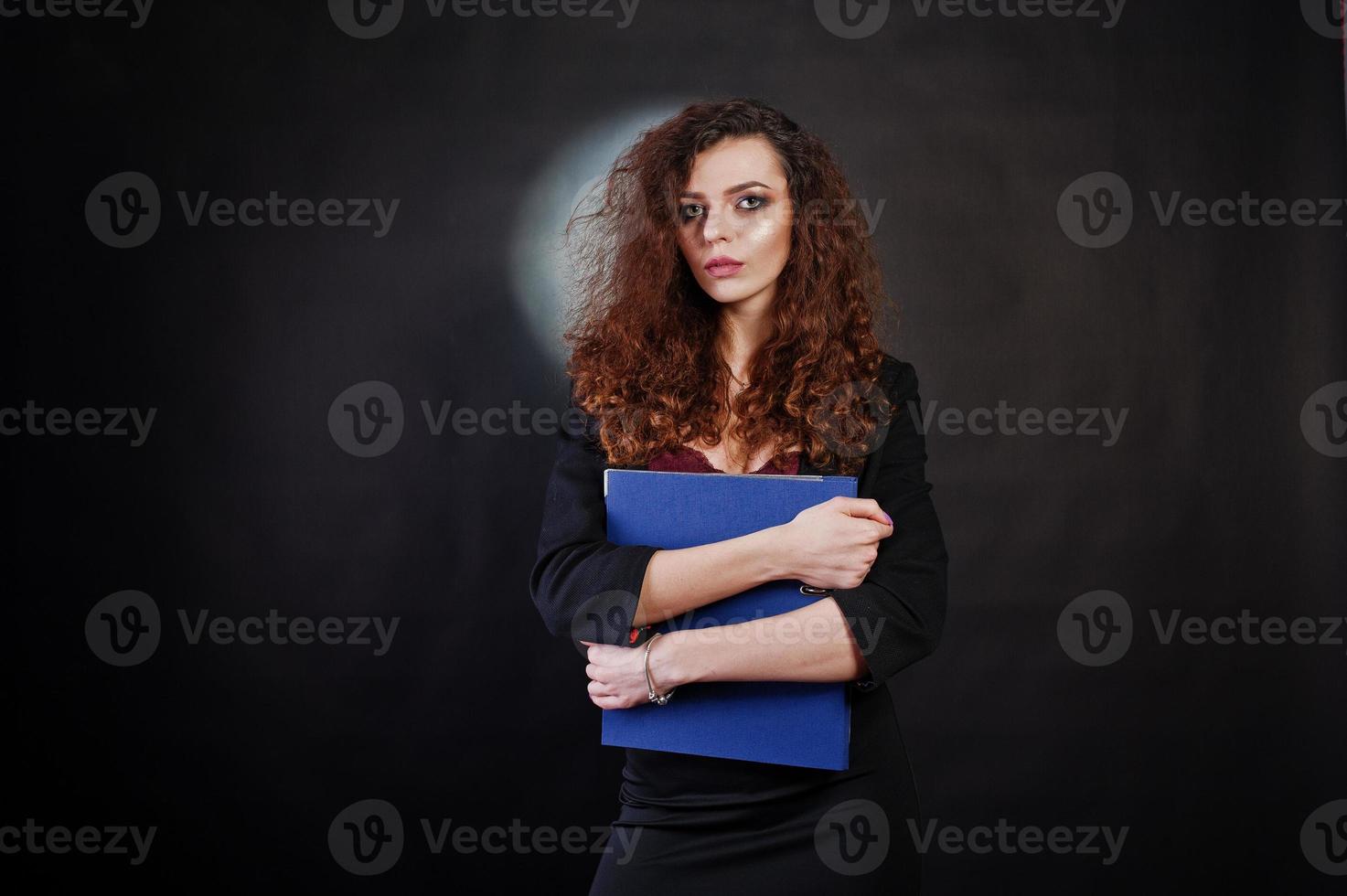 brünettes lockiges Mädchen in schwarzer Bürojacke mit Rock, auf BH mit Ordner mit Dokumenten in Händen auf Studio vor schwarzem Hintergrund. sexy Geschäftsfrau. foto