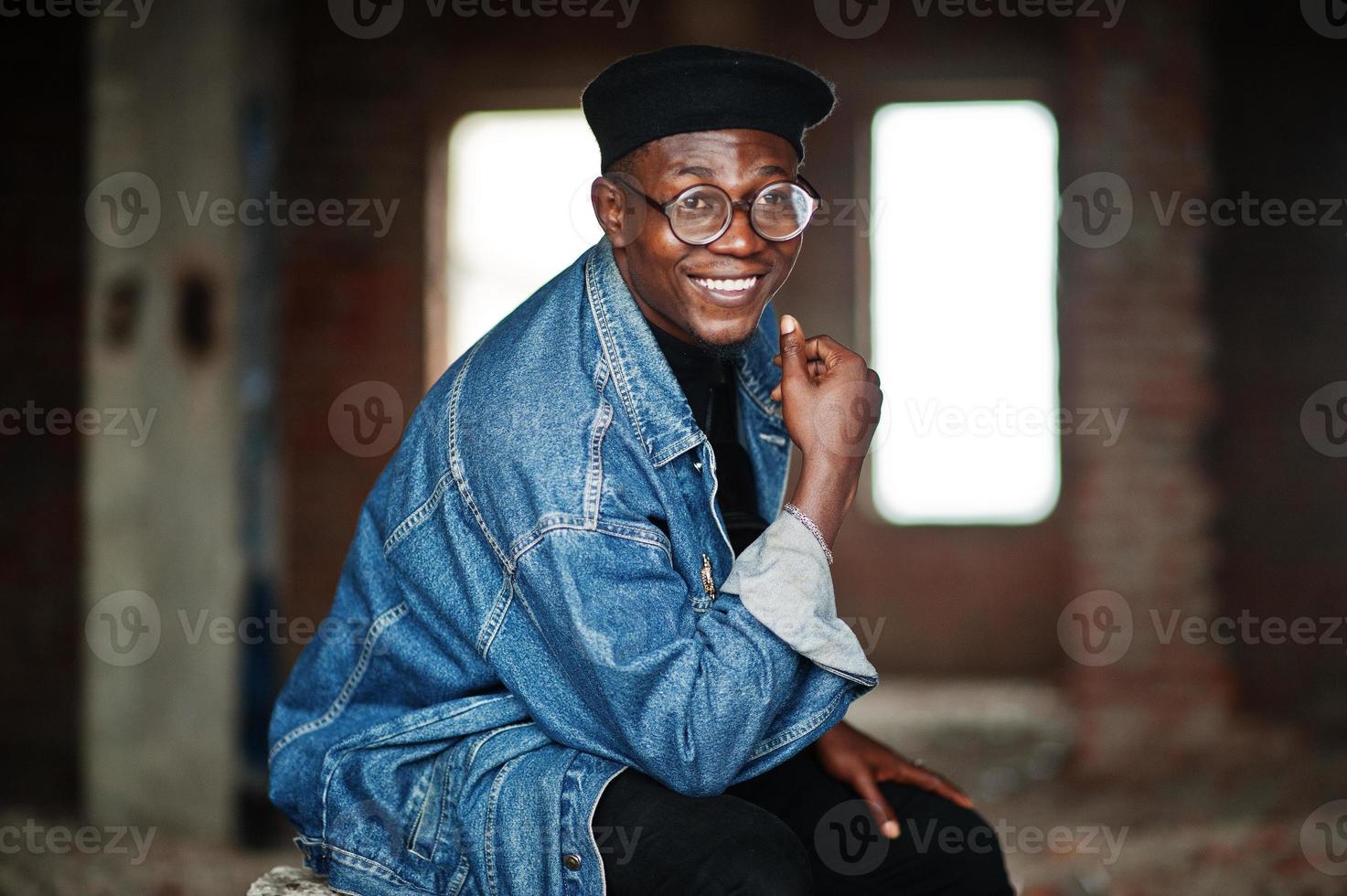 afroamerikanischer Mann in Jeansjacke, Baskenmütze und Brille in verlassener Ziegelei. foto