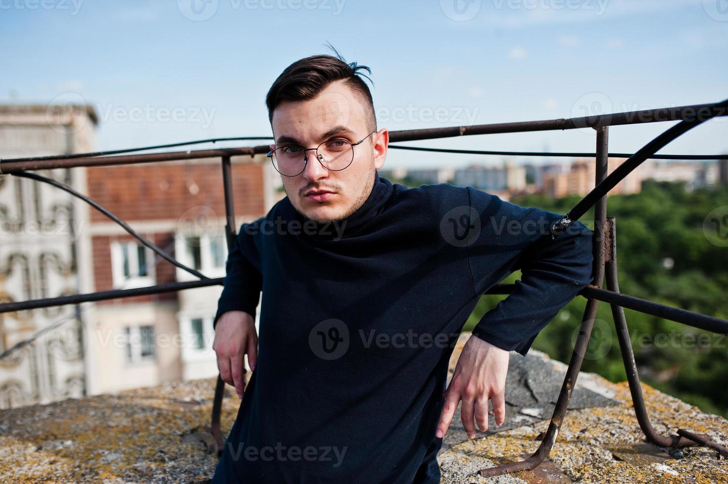 Träumer stylischer Macho in schwarzem Golf und Brille posiert auf dem Dach. foto