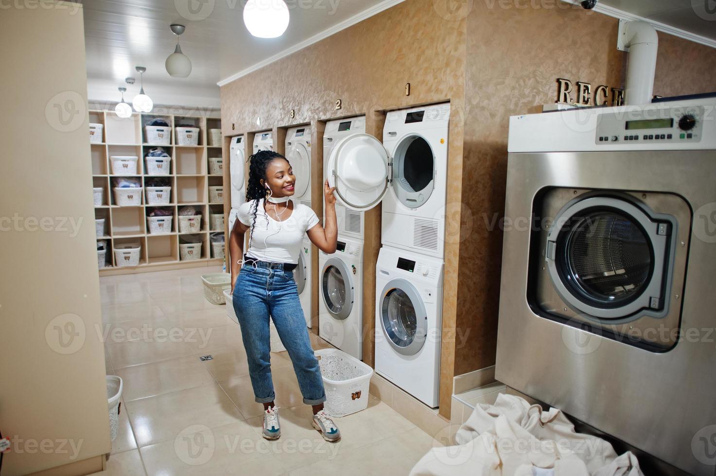 Fröhliche afroamerikanische Frau in der Nähe der Waschmaschine in der Selbstbedienungswäscherei. foto