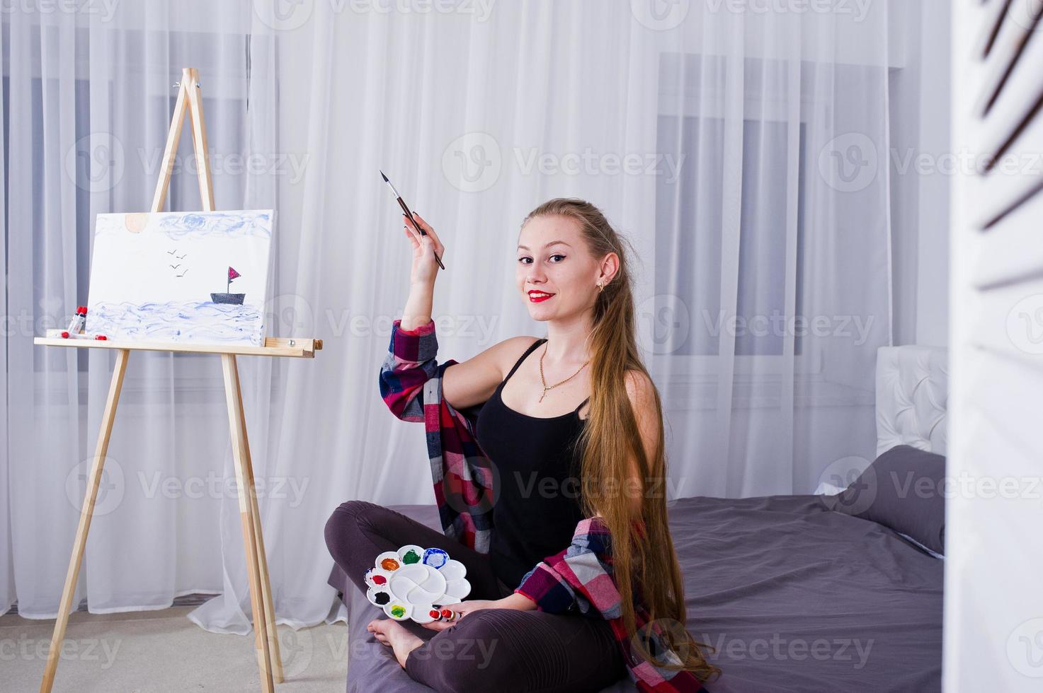 Schöne Künstlerin Malerin mit Pinsel und Ölleinwand posiert im Bett im Zimmer. foto