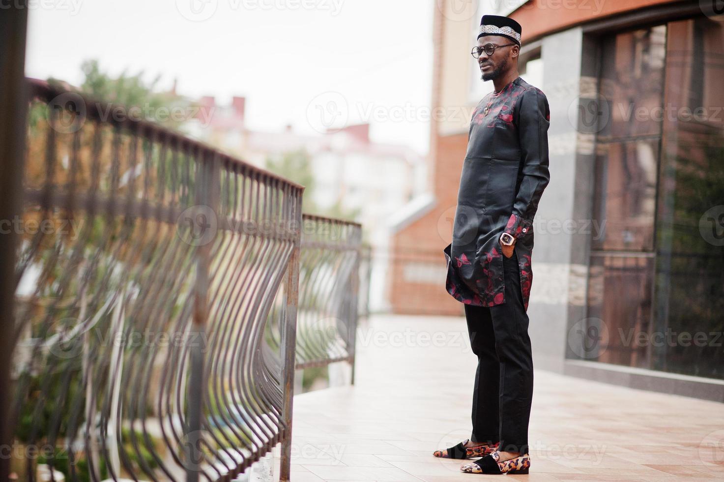 Schöner afroamerikanischer Mann mit traditioneller Kleidung, Mütze und Brille in der modernen Stadt. foto