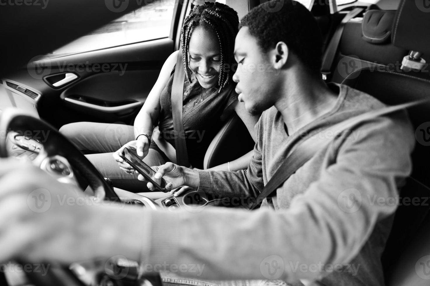 Schönes junges afroamerikanisches Paar, das auf den Beifahrersitzen sitzt, während ein gutaussehender Mann ein Auto fährt. Blick auf die Karte am Telefon. foto