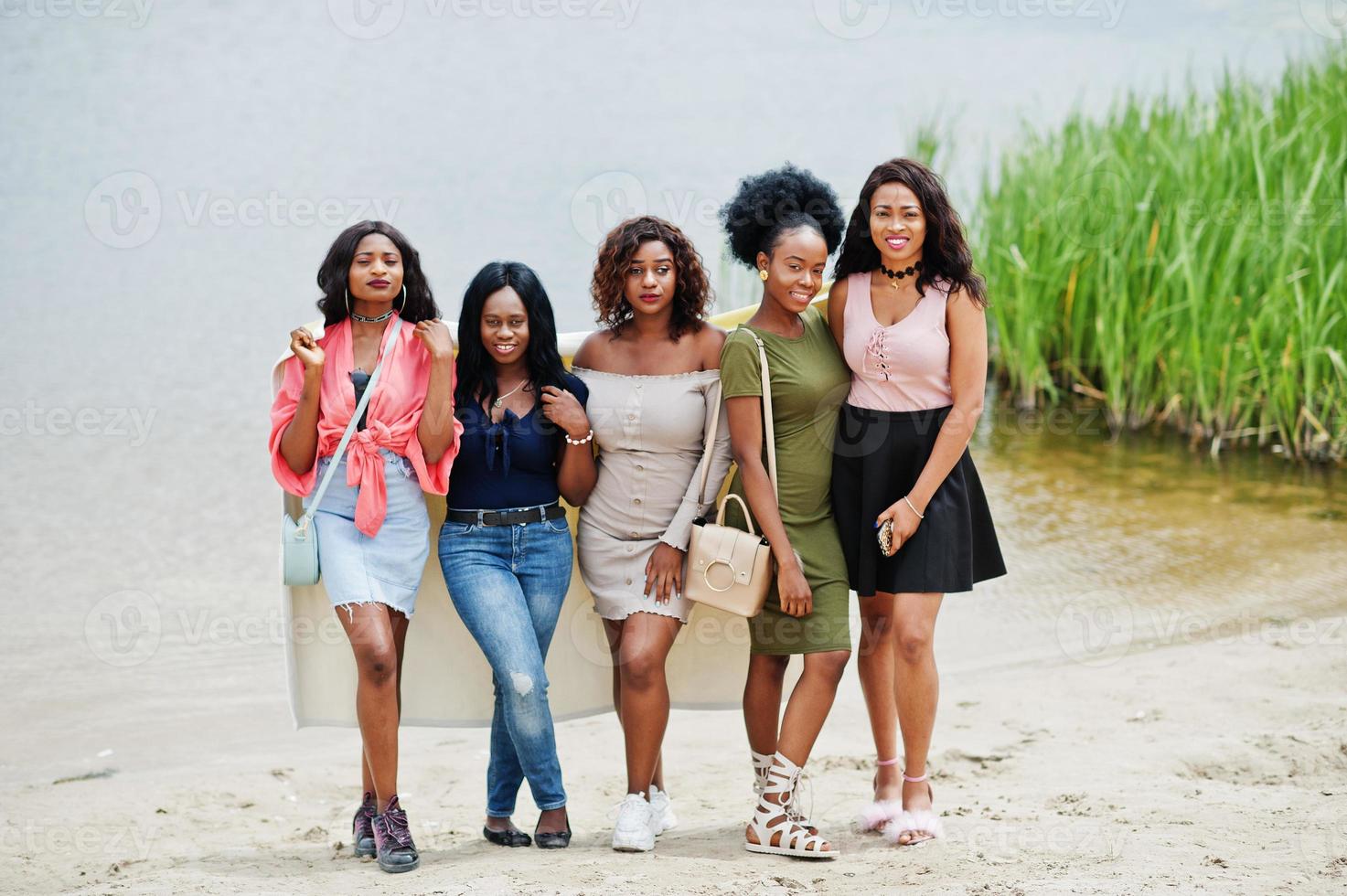 Gruppe von fünf afroamerikanischen Mädchen, die am Sand gegen den See stehen. foto