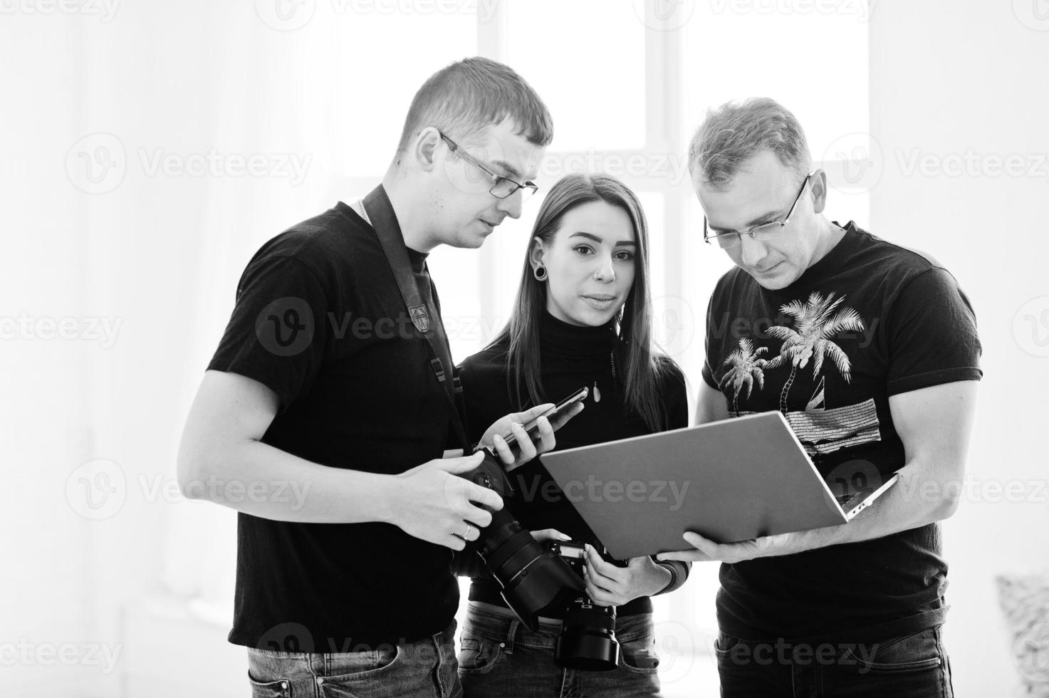 Fotograf erklärt seinem Team im Studio die Aufnahme und schaut auf den Laptop. im Gespräch mit seinen Assistenten, die während eines Fotoshootings eine Kamera halten. Teamarbeit und Brainstorming. foto