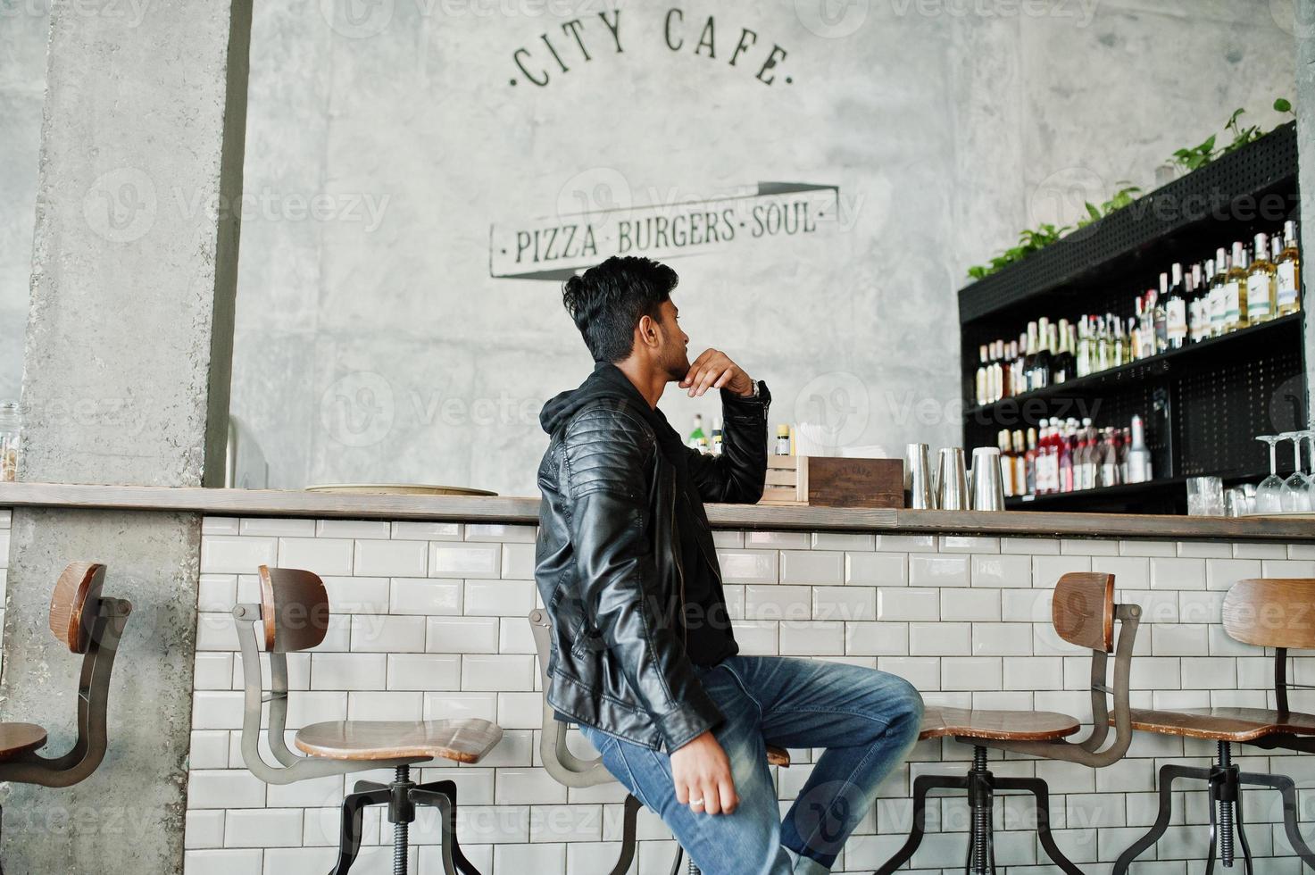 lässiger und stilvoller junger asiatischer mann trägt eine lederjacke, die an der bar sitzt, und wählt aus, was zu trinken ist. foto