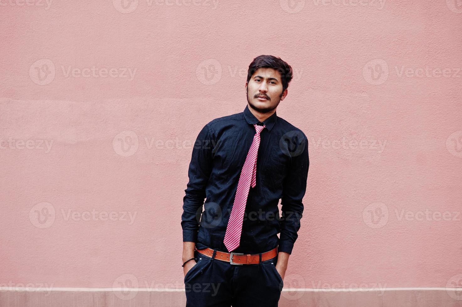 junger indischer mann auf schwarzem hemd und krawatte posierte vor rosa wand. foto